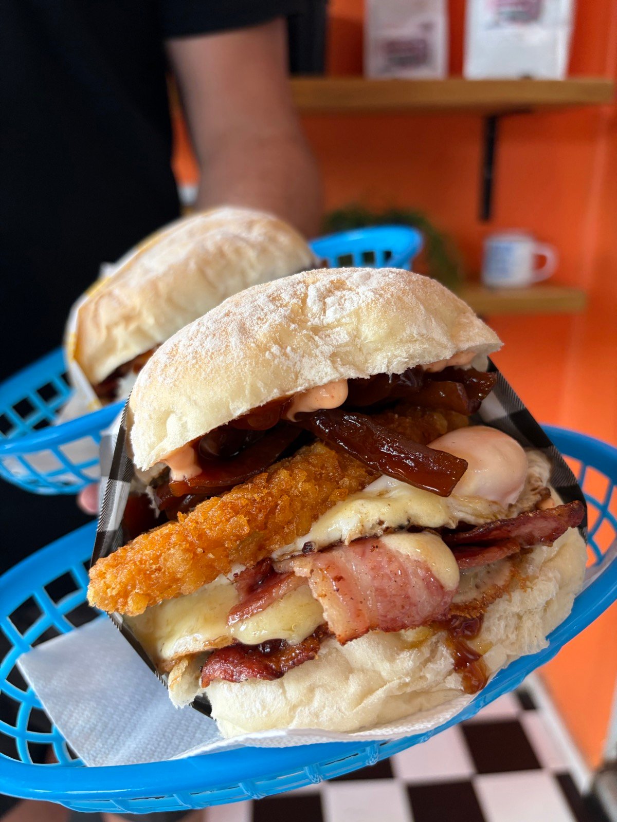 Loaded bacon, hash brown and egg roll with BBQ sauce in a blue basket, held up against the orange shop wall.